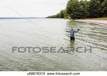 Stock Photo - Mature man standing in sea, holding camera. Fotosearch