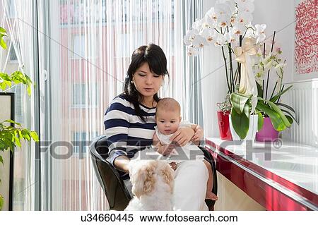 Stock Photography - Mature woman and baby granddaughter petting dog in kitchen. Fotosearch