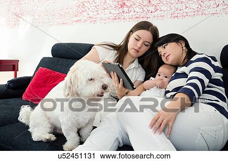 Stock Image - Mature woman and daughter with baby girl reading digital tablet on sofa. Fotosearch