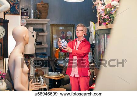 Stock Photo - Mature woman examining china pot in vintage shop. Fotosearch