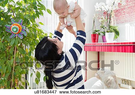 Mature woman holding up baby granddaughter in kitchen View Large Photo Image Stock Photo - Mature woman holding up baby granddaughter in kitchen. Fotosearch