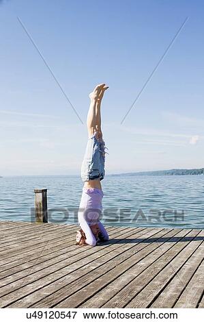 Stock Photo - Mature woman on pier by ocean balancing on head. Fotosearch