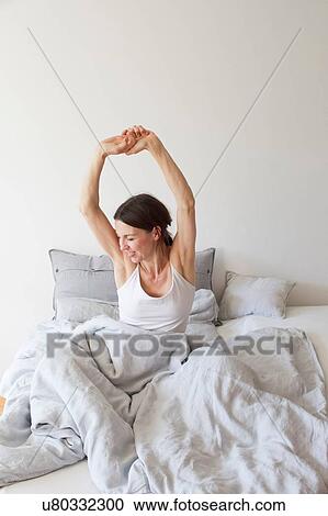 Mature woman wearing vest sitting in bed underneath quilt arms raised stretching View Large Photo Image Stock Image - Mature woman wearing vest sitting in bed underneath quilt arms raised stretching. Fotosearch