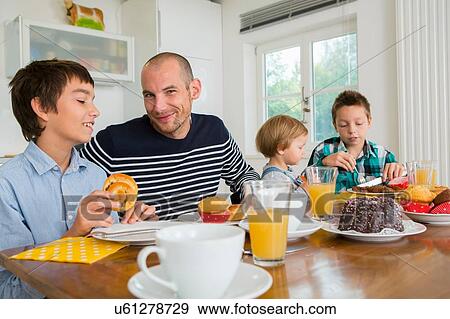 Stock Photo - Mid adult man and family having tea at kitchen table. Fotosearch