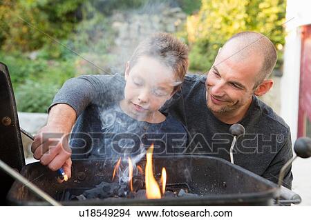 Picture - Mid adult man and son lighting barbecue in garden. Fotosearch
