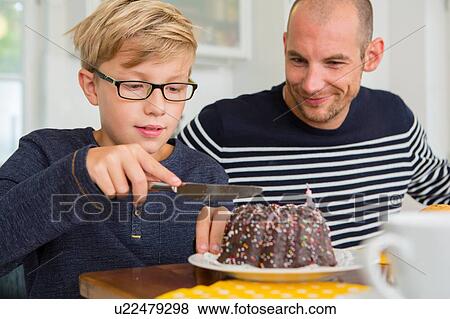 Mid adult man and son slicing cake at kitchen table View Large Photo Image Stock Photo - Mid adult man and son slicing cake at kitchen table. Fotosearch