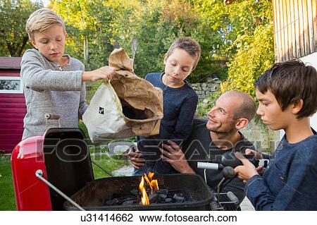 Stock Image - Mid adult man and sons preparing barbecue in garden. Fotosearch