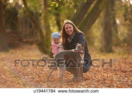 Mid adult woman and baby daughter petting dog in autumn park View Large Photo Image Picture - Mid adult woman and baby daughter petting dog in autumn park. Fotosearch
