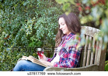 Stock Photo - Mid adult woman reading on garden bench at Thornbury Castle, South Gloucestershire, UK. Fotosearch