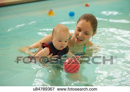 Stock Photo - Mother and baby daughter in swimming pool playing with ball. Fotosearch