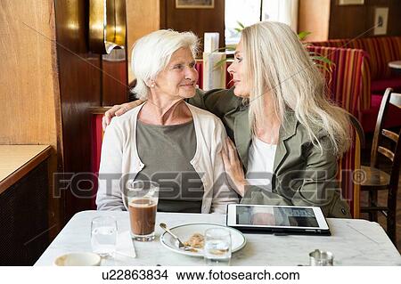 Mother and daughter sitting together in cafe, daughter's arm around mother, digital tablet on table View Large Photo Image Picture - Mother and daughter sitting together in cafe, daughter's arm around mother, digital tablet on table. Fotosearch