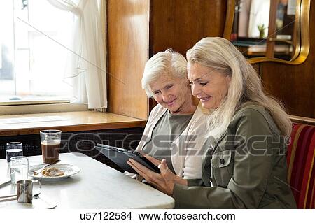 Picture - Mother and daughter sitting together in cafe, looking at digital tablet. Fotosearch