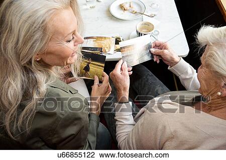 Mother and daughter sitting together in cafe, looking at photographs, rear view View Large Photo Image Stock Image - Mother and daughter sitting together in cafe, looking at photographs, rear view. Fotosearch