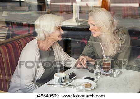 Mother and daughter sitting together in cafe, holding hands, seen through cafe window View Large Photo Image Stock Photo - Mother and daughter sitting together in cafe, holding hands, seen through cafe window. Fotosearch