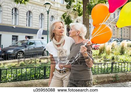 Mother and daughter walking along street together, holding bunch of balloons View Large Photo Image Stock Photo - Mother and daughter walking along street together, holding bunch of balloons. Fotosearch