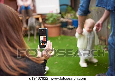 Mother in garden using smartphone to film daughter learning to walk, focus on foreground View Large Photo Image Stock Image - Mother in garden using smartphone to film daughter learning to walk, focus on foreground. Fotosearch