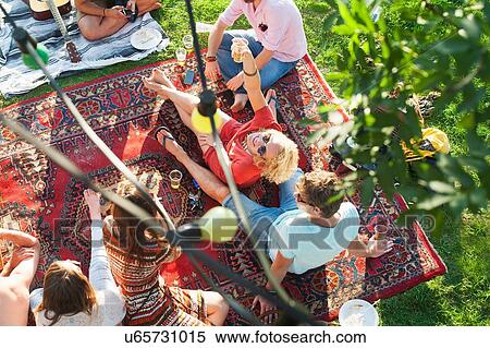 Stock Photography - Overhead view of group of friends relaxing on rug at sunset park party. Fotosearch