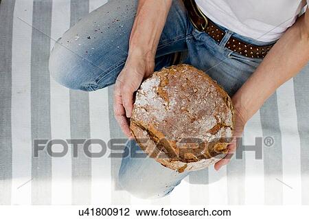 Stock Image - Overhead view of mature woman on striped rug holding fresh baked bread. Fotosearch