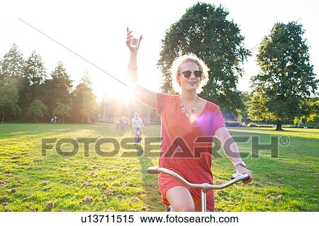 Party going woman holding up wine arriving in park on bicycle at sunset View Large Photo Image Stock Photography - Party going woman holding up wine arriving in park on bicycle at sunset. Fotosearch