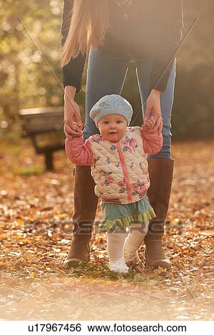 Stock Photograph - Portrait of baby girl holding mothers hands in autumn park. Fotosearch