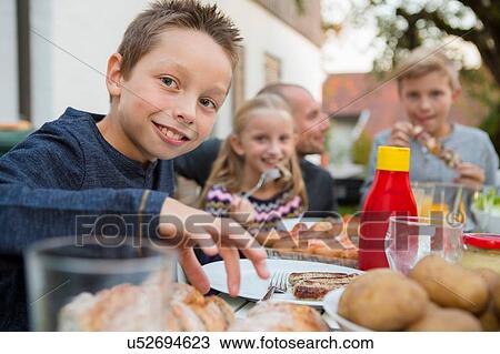 Stock Image - Portrait of boy and family at garden barbecue table. Fotosearch