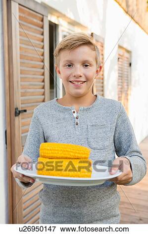 Portrait of boy carrying plate of corn cobs for barbecue in garden View Large Photo Image Stock Photo - Portrait of boy carrying plate of corn cobs for barbecue in garden. Fotosearch