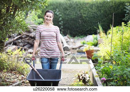 Stock Photo - Portrait of female gardener pushing wheelbarrow in rustic organic garden. Fotosearch