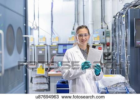 Stock Image - Portrait of female scientist holding lithium ion pouch battery in battery research facility. Fotosearch