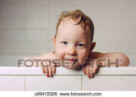 Stock Photograph - Portrait of girl with wet hair in bath holding onto edge looking at camera smiling. Fotosearch