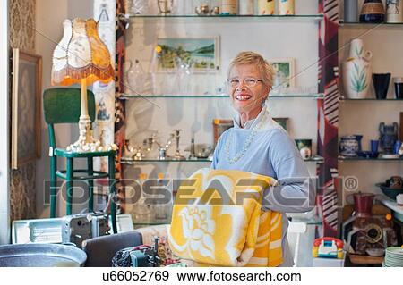 Stock Photo - Portrait of mature woman folding yellow blanket in vintage shop. Fotosearch