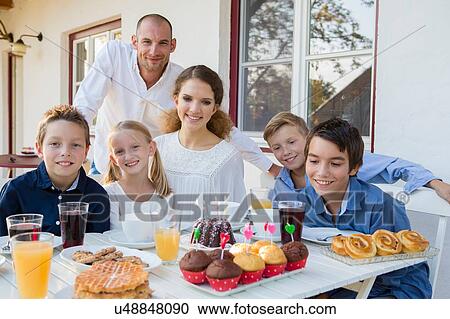 Stock Image - Portrait of mid adult man and family with birthday cake at patio table. Fotosearch