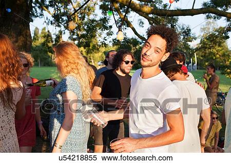 Stock Photography - Portrait of mid adult man at crowded sunset party in park. Fotosearch