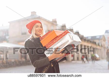 Stock Image - Portrait of stylish young woman carrying stack of christmas gifts, Covent Garden, London, UK. Fotosearch