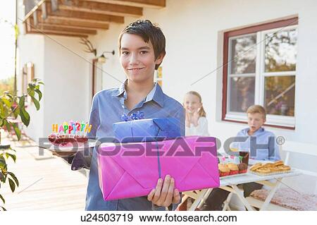 Portrait of teenage boy carrying birthday cake and birthday gifts on patio View Large Photo Image Stock Photo - Portrait of teenage boy carrying birthday cake and birthday gifts on patio. Fotosearch