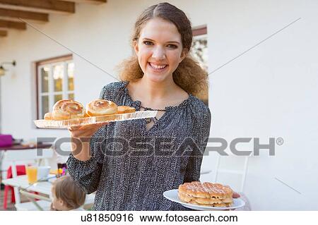 Stock Photograph - Portrait of teenage girl carrying party food on patio. Fotosearch