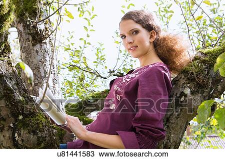 Stock Image - Portrait of teenage girl reading in garden tree. Fotosearch