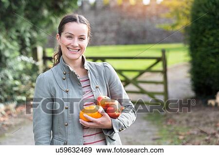 Stock Photo - Portrait of woman holding apples and pumpkin at Thornbury Castle, South Gloucestershire, UK. Fotosearch