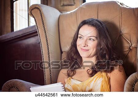 Stock Image - Portrait of woman sitting in old armchair at Thornbury Castle, South Gloucestershire, UK. Fotosearch