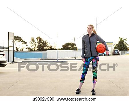 Stock Image - Portrait of young female basketball player in parking lot. Fotosearch
