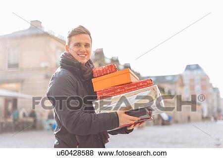 Stock Photo - Portrait of young man carrying stack of xmas presents in Covent Garden, London, UK. Fotosearch