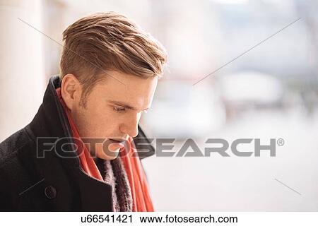 Stock Image - Portrait of young man in city looking down. Fotosearch
