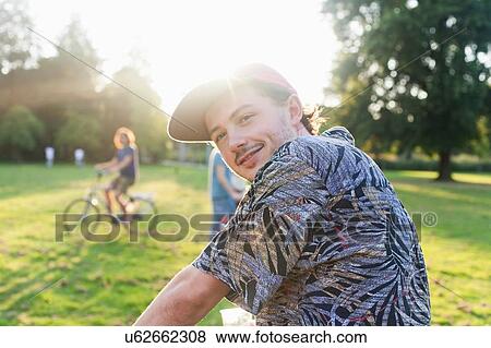 Stock Photo - Portrait of young man looking over his shoulder in sunlit park. Fotosearch
