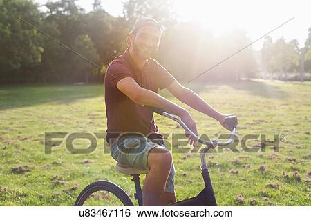 Stock Photograph - Portrait of young man on bicycle in sunlit park. Fotosearch