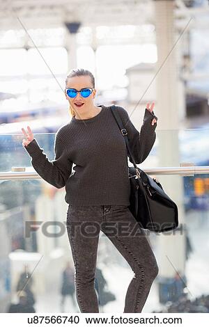 Stock Image - Portrait of young woman, gesturing peace sign, outdoors. Fotosearch