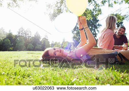 Portrait of young woman lying on grass with balloon at park party View Large Photo Image Stock Image - Portrait of young woman lying on grass with balloon at park party. Fotosearch