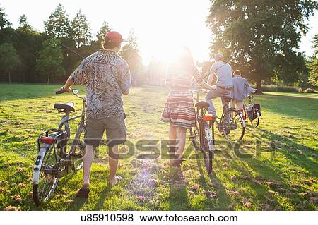Stock Photo - Rear view of adult partygoers arriving on bicycles to sunset park party. Fotosearch