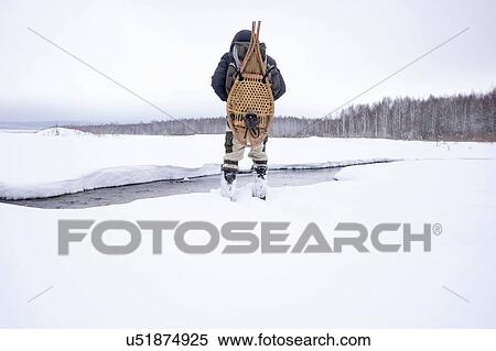 Rear view of mid adult man in snow covered field by river carrying traditional snowshoes, Ural, Russia View Large Photo Image Stock Photography - Rear view of mid adult man in snow covered field by river carrying traditional snowshoes, Ural, Russia. Fotosearch