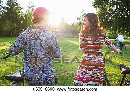 Rear view of partygoing couple arriving on bicycles to sunset park party View Large Photo Image Stock Image - Rear view of partygoing couple arriving on bicycles to sunset park party. Fotosearch