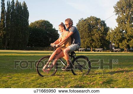 Stock Image - Romantic young couple on bicycle together in park. Fotosearch