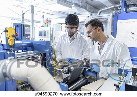 Stock Image - Scientists with lithium ion battery production line in battery research facility. Fotosearch